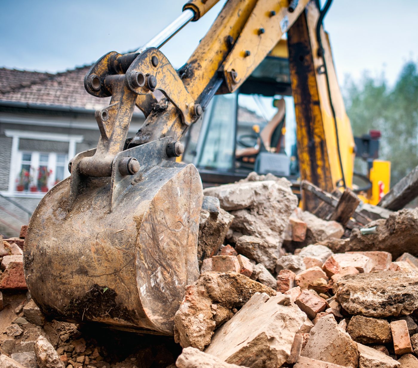 Excavator bucket on a pile of brick and concrete rubble from a demolished house